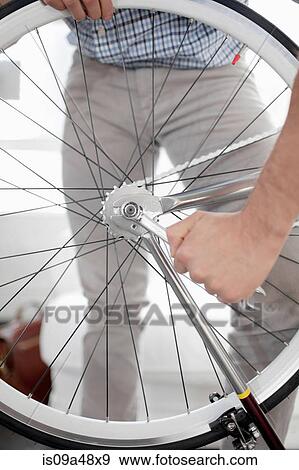Stock Photo - Man fixing bicycle wheel indoors. Fotosearch