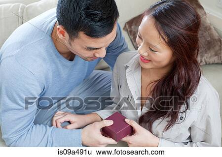 Stock Photograph - Man giving girlfriend gift on sofa. Fotosearch