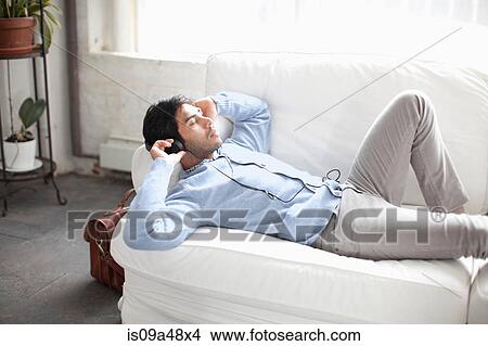 Man listening to headphones on sofa View Large Photo Image Picture - Man listening to headphones on sofa. Fotosearch