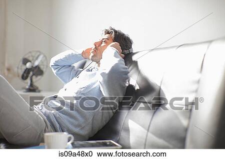Stock Image - Man listening to headphones on sofa. Fotosearch