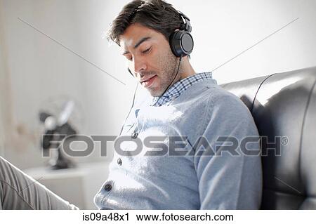 Stock Image - Man listening to headphones on sofa. Fotosearch