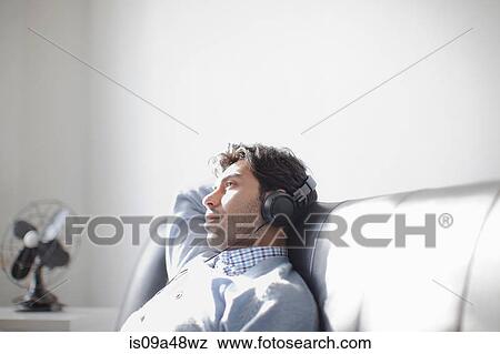 Stock Photo - Man listening to headphones on sofa. Fotosearch