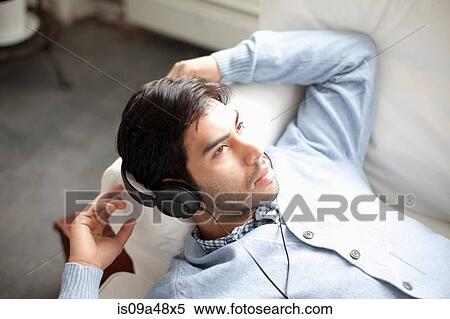 Stock Photography - Man listening to headphones on sofa. Fotosearch