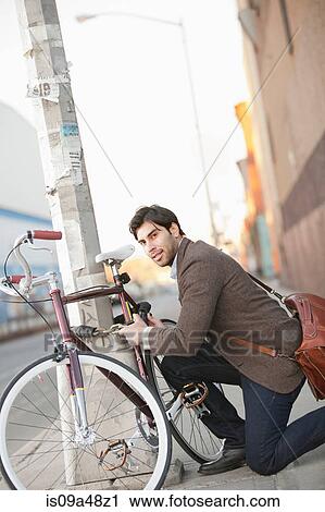 Man locking bicycle on city street View Large Photo Image Stock Image - Man locking bicycle on city street. Fotosearch