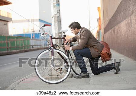 Stock Image - Man locking bicycle on city street. Fotosearch