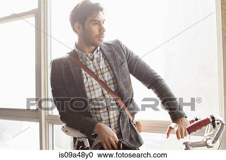 Stock Image - Man standing with bicycle by window. Fotosearch