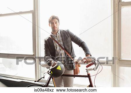 Stock Photo - Man standing with bicycle by window. Fotosearch