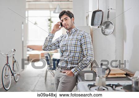 Stock Image - Man talking on cell phone in kitchen. Fotosearch