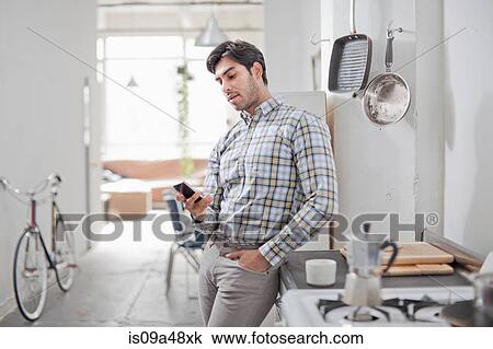Stock Image - Man using cell phone in kitchen. Fotosearch