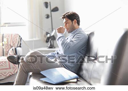 Stock Photo - Man using laptop on sofa. Fotosearch