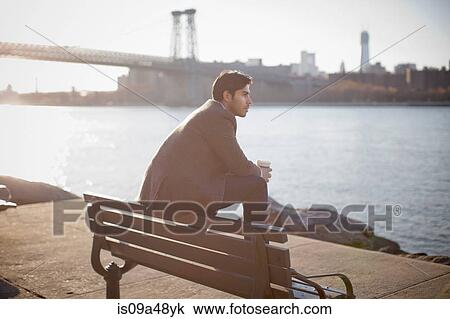 Stock Image - Man with cup of coffee on park bench. Fotosearch