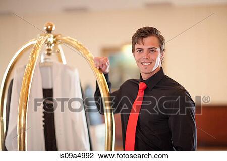 Stock Image - Porter with luggage cart in hotel lobby. Fotosearch