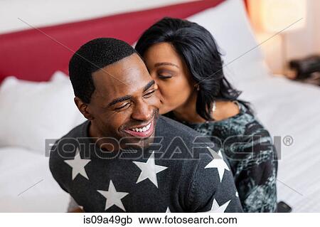 Stock Image - Smiling couple sitting on bed. Fotosearch