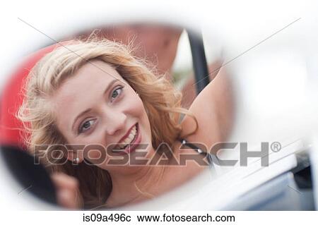 Stock Image - Smiling woman reflected in car mirror. Fotosearch