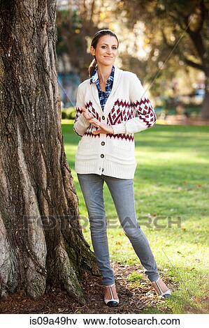 Smiling woman standing by tree View Large Photo Image Stock Photo - Smiling woman standing by tree. Fotosearch
