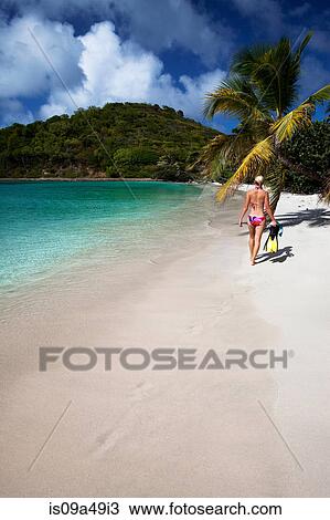 Stock Image - Woman carrying fins on tropical beach. Fotosearch