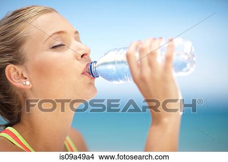 Picture - Woman drinking water bottle outdoors. Fotosearch