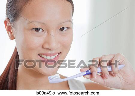Picture - Woman holding toothbrush in bathroom. Fotosearch