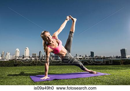 Stock Image - Woman practicing yoga in urban park. Fotosearch