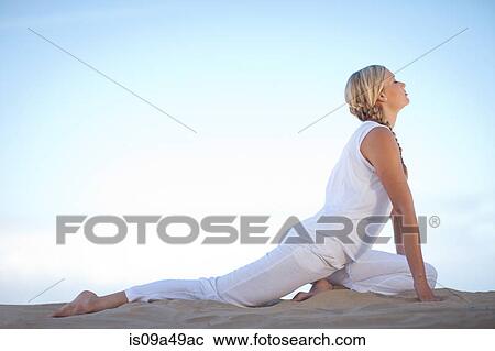 Stock Image - Woman practicing yoga on beach. Fotosearch