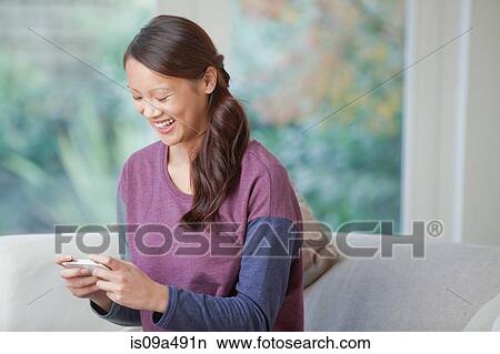 Picture - Woman using cell phone on sofa. Fotosearch