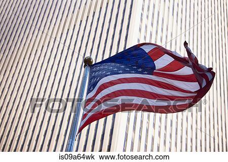 Stock Image - American flag flying by city skyscraper. Fotosearch