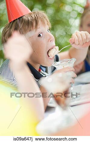 Stock Image - Boy having ice cream sundae at party. Fotosearch