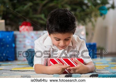 Boy holding Christmas present on floor View Large Photo Image Stock Photograph - Boy holding Christmas present on floor. Fotosearch