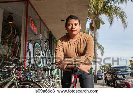 Stock Image - Boy leaning on bicycle outside shop. Fotosearch