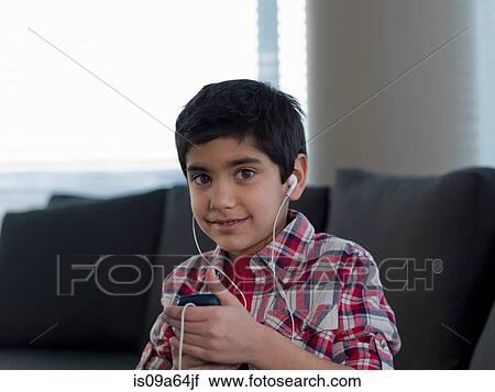 Stock Image - Boy listening to earphones indoors. Fotosearch