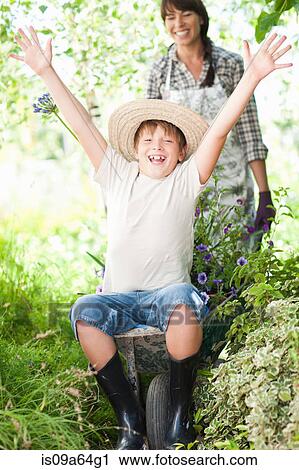 Stock Image - Boy sitting in wheelbarrow of plants. Fotosearch