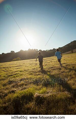 Stock Image - Boys running in grassy field. Fotosearch