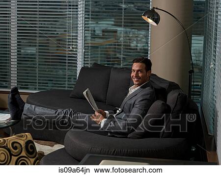 Businessman reading newspaper on sofa View Large Photo Image Picture - Businessman reading newspaper on sofa. Fotosearch