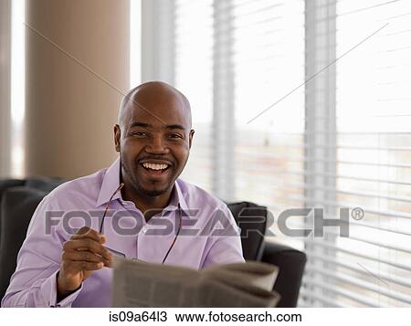 Stock Image - Businessman reading newspaper on sofa. Fotosearch