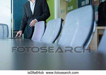 Stock Image - Businessman standing at conference desk. Fotosearch