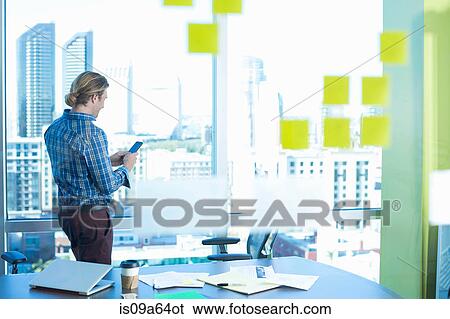 Stock Photograph - Businessman using cell phone at window. Fotosearch