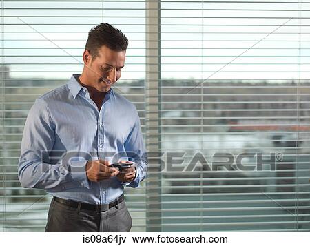 Stock Photo - Businessman using cell phone by window. Fotosearch