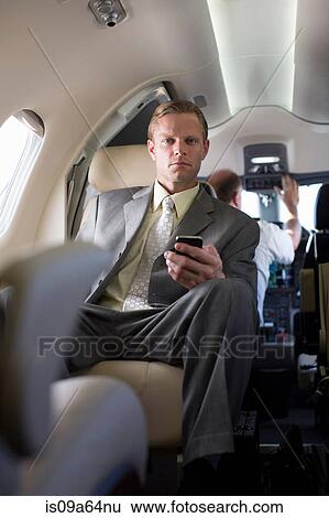 Stock Photograph - Businessman using cell phone on airplane. Fotosearch