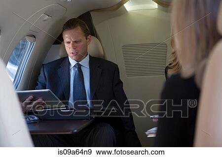 Businessman using tablet on airplane View Large Photo Image Stock Photo - Businessman using tablet on airplane. Fotosearch