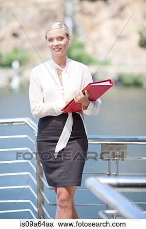 Stock Image - Businesswoman carrying folder on balcony. Fotosearch