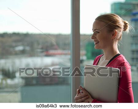 Businesswoman holding laptop by window View Large Photo Image Stock Image - Businesswoman holding laptop by window. Fotosearch
