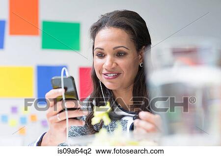 Stock Image - Businesswoman listening to earphones. Fotosearch