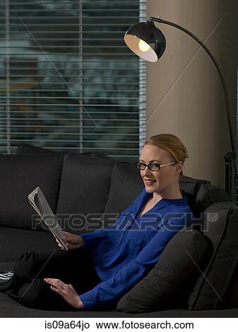 Picture - Businesswoman reading newspaper on sofa. Fotosearch