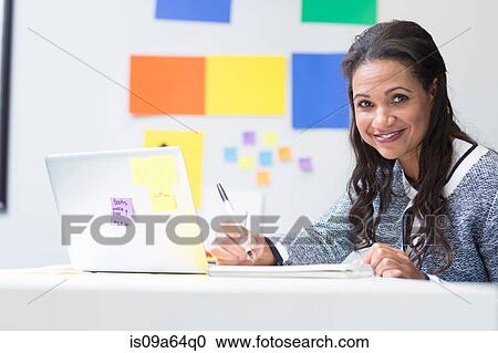 Stock Image - Businesswoman taking notes at desk. Fotosearch