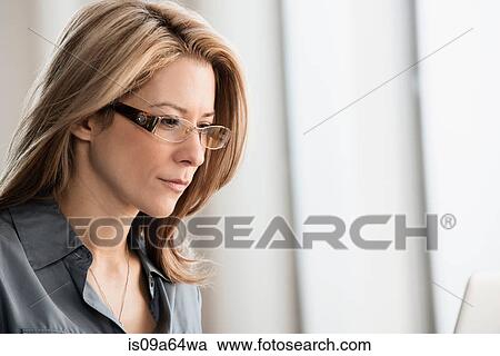 Stock Image - Businesswoman wearing glasses in office. Fotosearch