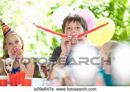 Stock Image - Children blowing noisemakers at party. Fotosearch