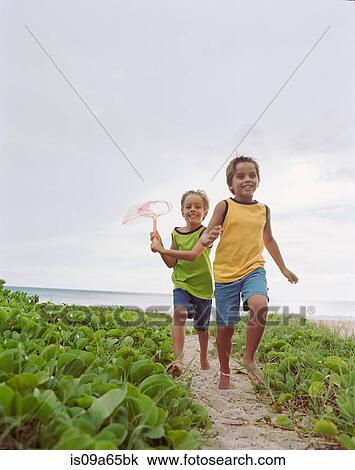 Stock Image - Children running together on beach. Fotosearch