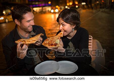 Stock Image - Couple eating pizza on city street. Fotosearch