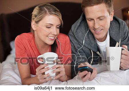 Couple listening to earphones on bed View Large Photo Image Stock Image - Couple listening to earphones on bed. Fotosearch