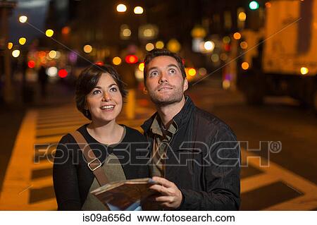 Stock Image - Couple reading city map at night. Fotosearch